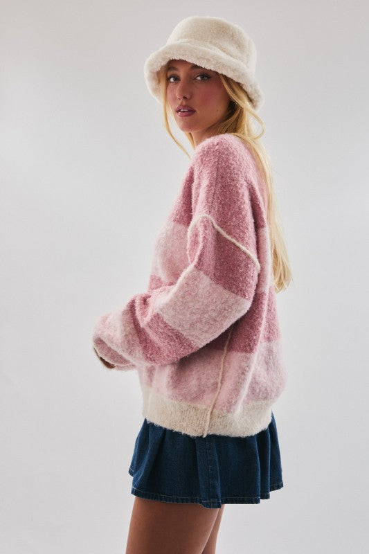 Woman wearing a pink and white sweater with a denim skirt on a plain background