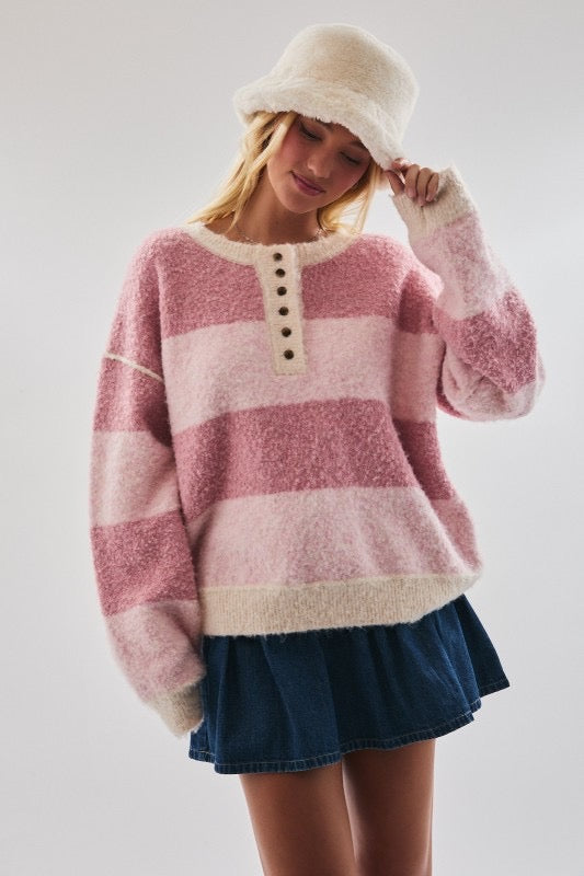 Woman wearing a pink and white striped sweater with a denim skirt on a plain background