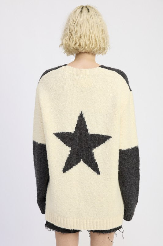 Person wearing a cream sweater with a black star design on a plain background
