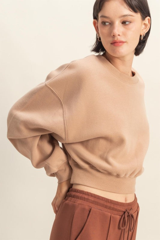 Woman wearing a beige sweater with puffed sleeves against a plain background