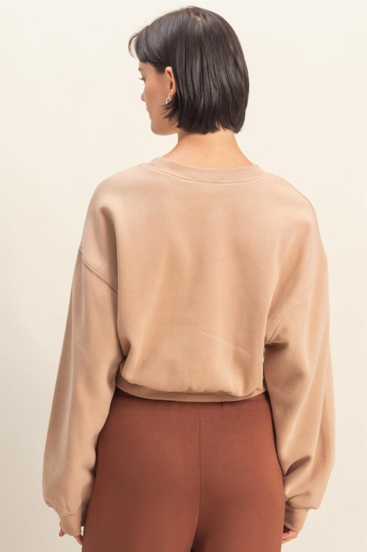Person wearing a beige sweatshirt and brown pants on a plain background