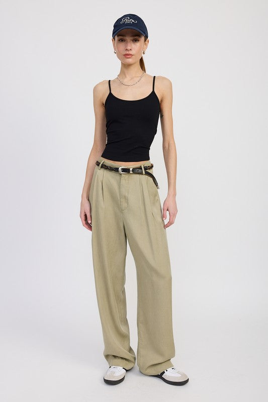Woman wearing a black tank top, beige wide-leg pants, and a navy cap on a white background
