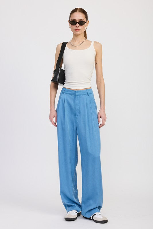 Woman wearing a white sleeveless top and blue high-waisted pants on a white background
