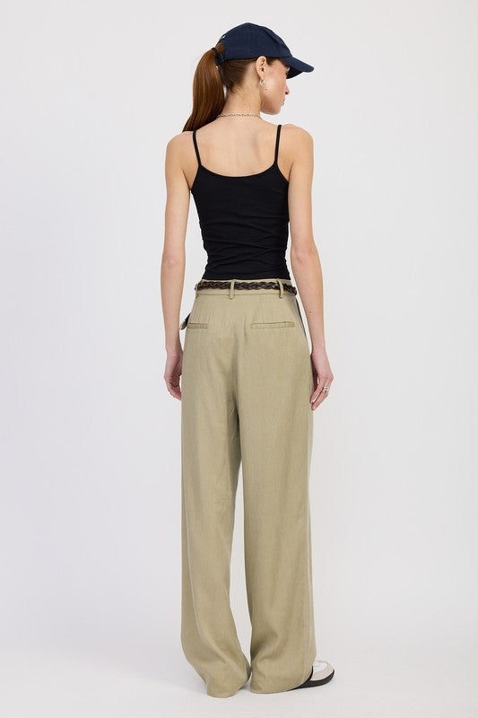 Woman wearing a black tank top and beige pants with a navy cap on a white background