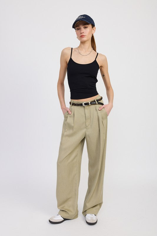Woman wearing a black tank top, beige wide-leg pants, and a cap on a white background