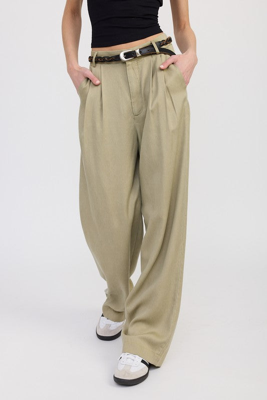 Person wearing beige wide-leg pants with a black top and white shoes on a light gray background