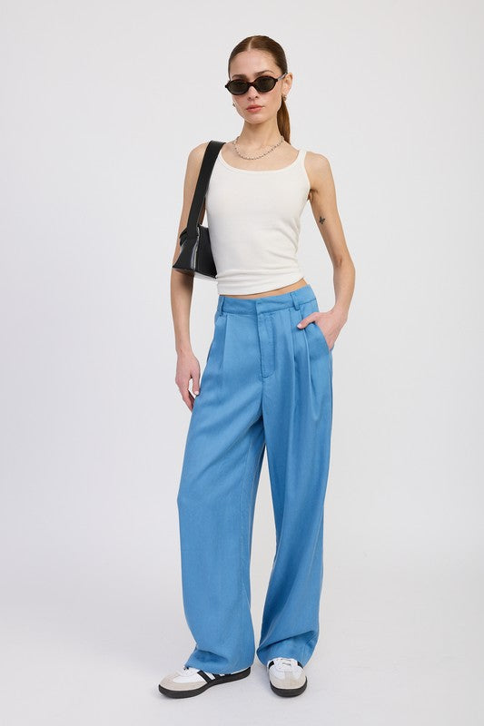 Woman wearing a white sleeveless top and blue high-waisted pants on a white background
