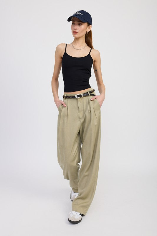 Woman wearing a black tank top, beige high-waisted pants, and a navy cap on a white background