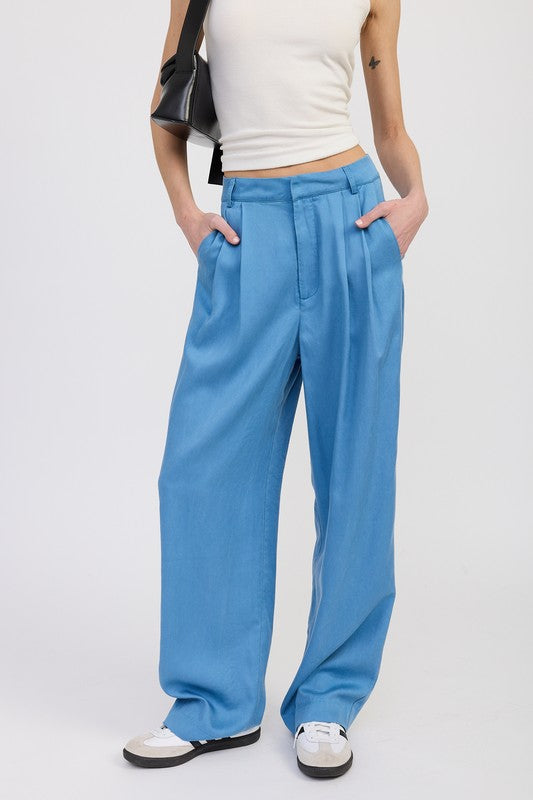 Person wearing blue wide-leg pants and a white top on a plain background