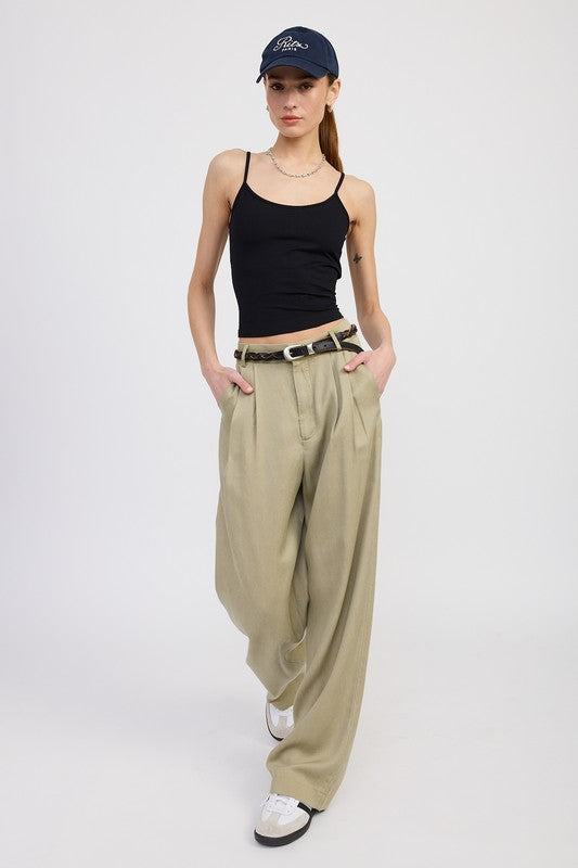 Woman wearing a black tank top, beige wide-leg pants, and a navy cap on a white background