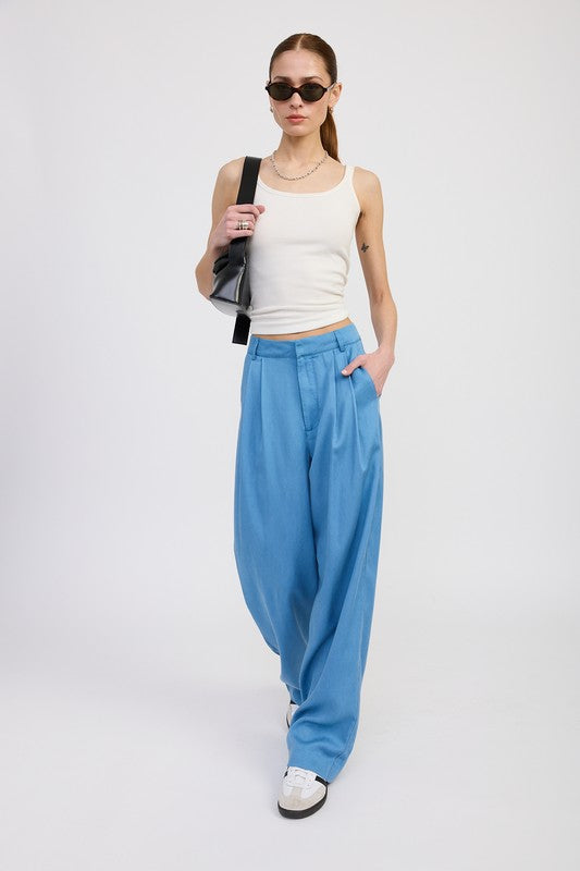 Woman wearing a white tank top and blue high-waisted pants on a white background