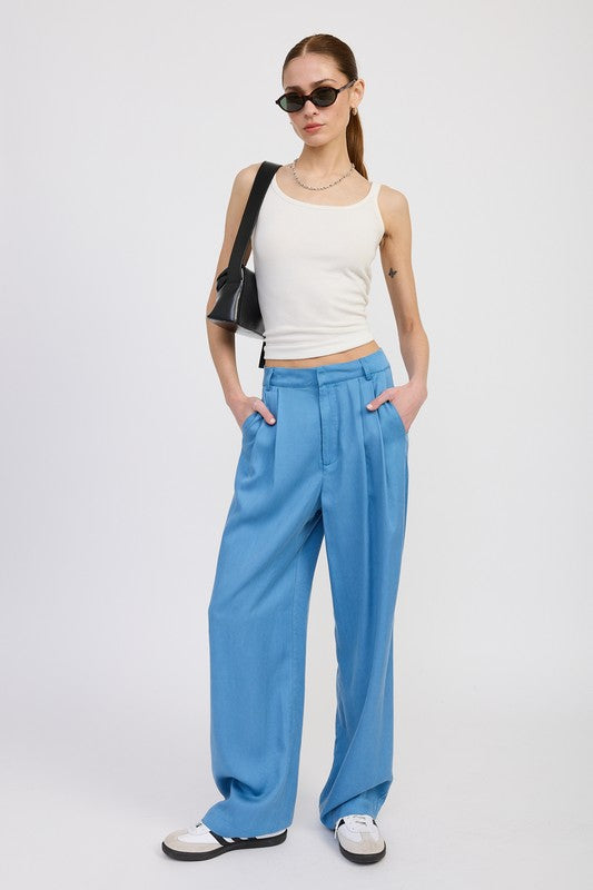 Woman wearing a white tank top and blue pants with sunglasses and a black bag on a white background