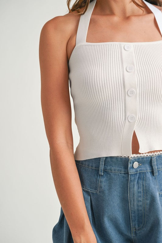 Woman wearing a white ribbed halter top and blue jeans.