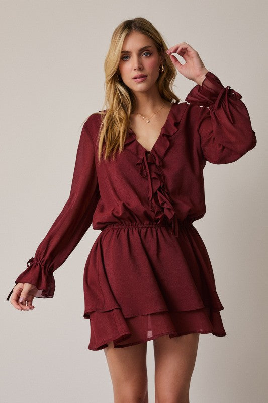 Woman wearing a burgundy dress with ruffled details on a neutral background